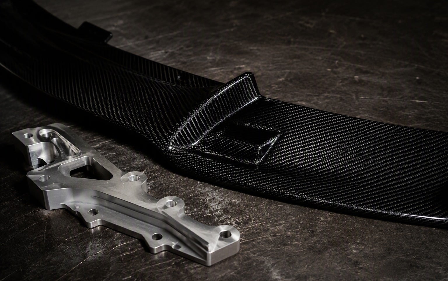 Carbon fiber automotive part next to machined aluminum part on a workbench