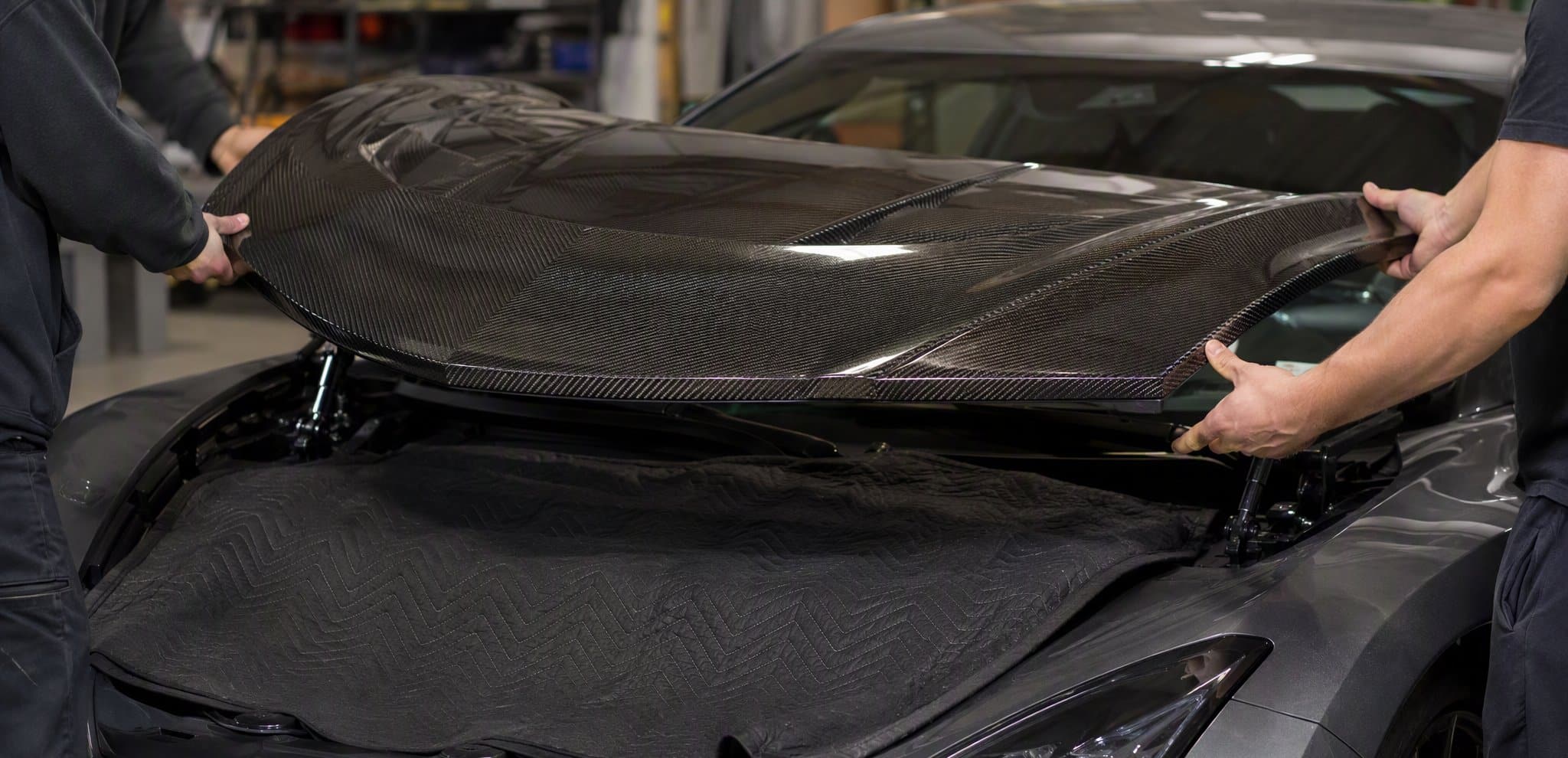 Two people lowering a carbon fiber hood onto the factory hinges
