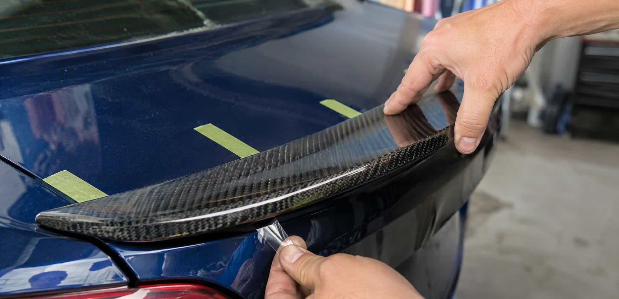 Pressing a carbon fiber ducktail spoiler onto the trunk with 3M tape