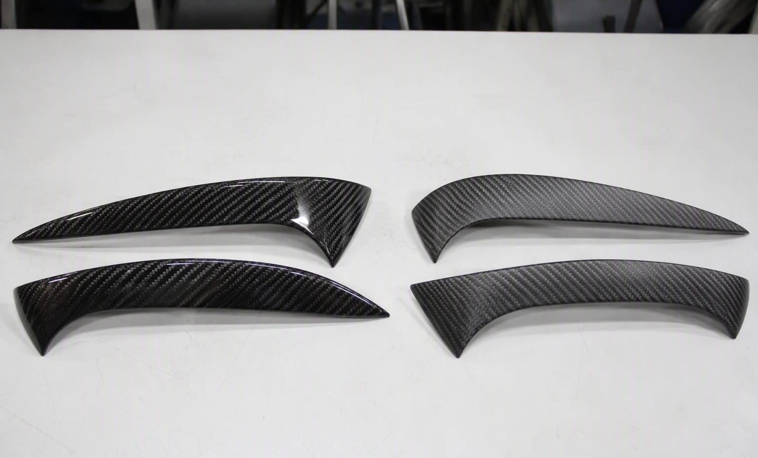 Gloss wet carbon headlight eyelids next to satin dry carbon pre-preg eyelids