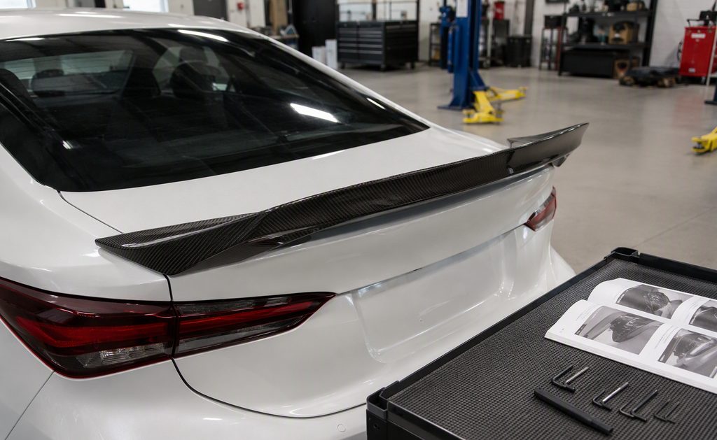 Carbon fiber rear spoiler test-fitted on a car trunk in a workshop